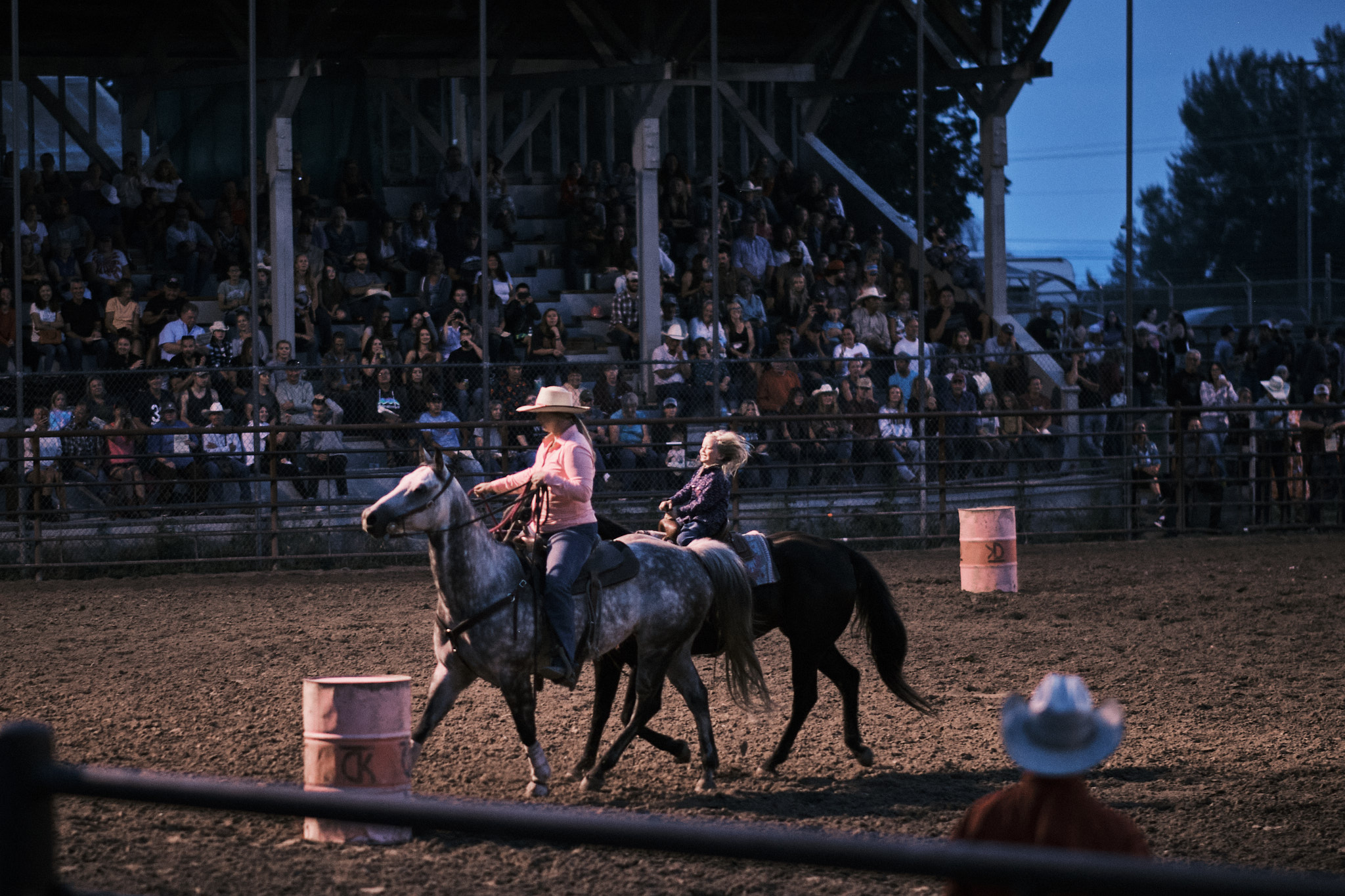 A momma cowgirl and her young cowgirl daughter barrel racing together