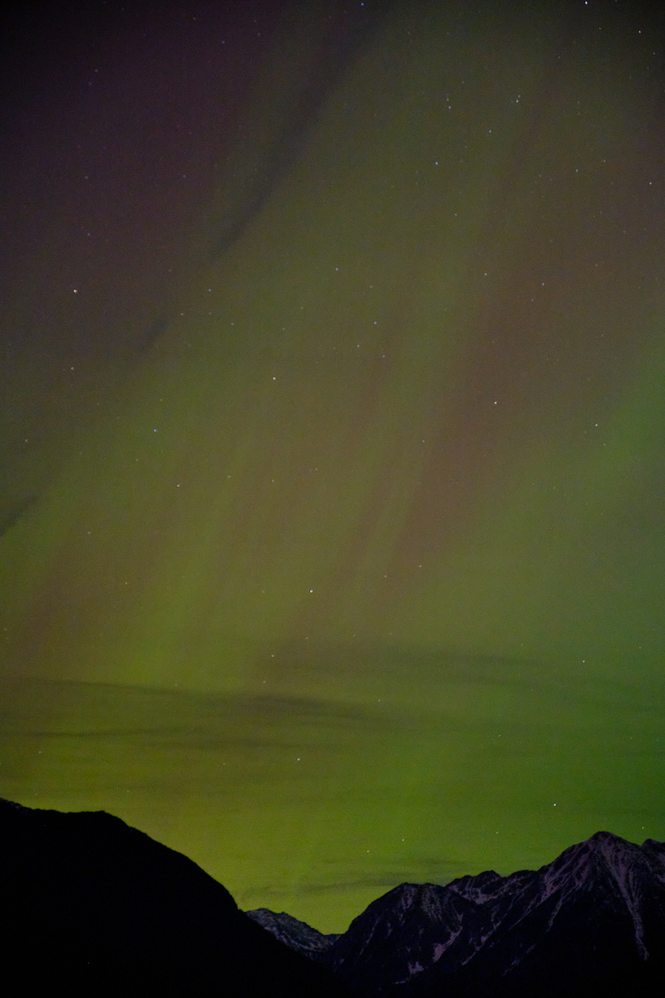 an aurora borealis over the mission mountains, the sky full of stars