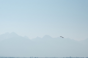 landscape of the mission mountains taken from ninepipes reservoir during mid-morning, the sky thick with smoke, a pair birds flying from right to left