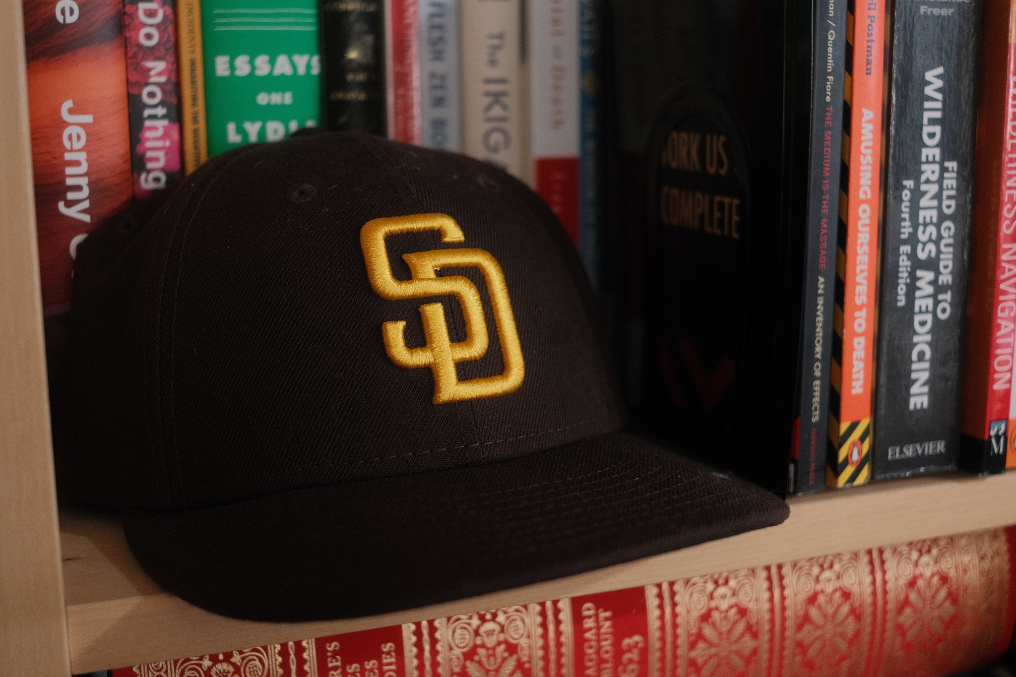 A San Diego Padres baseball sits on a bookshelf beside a stack of books and in front of other books