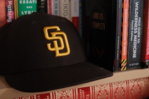 A San Diego Padres baseball sits on a bookshelf beside a stack of books and in front of other books