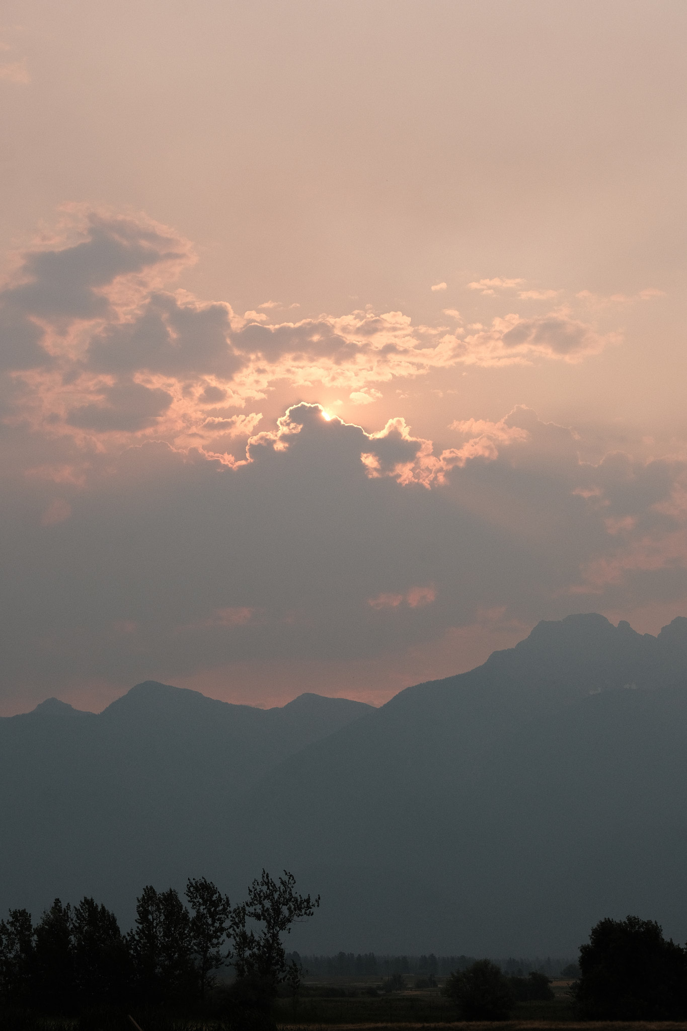 a view of the mid-morning mission mountains thick with a red and smokey haze, the red sun peeking through some clouds