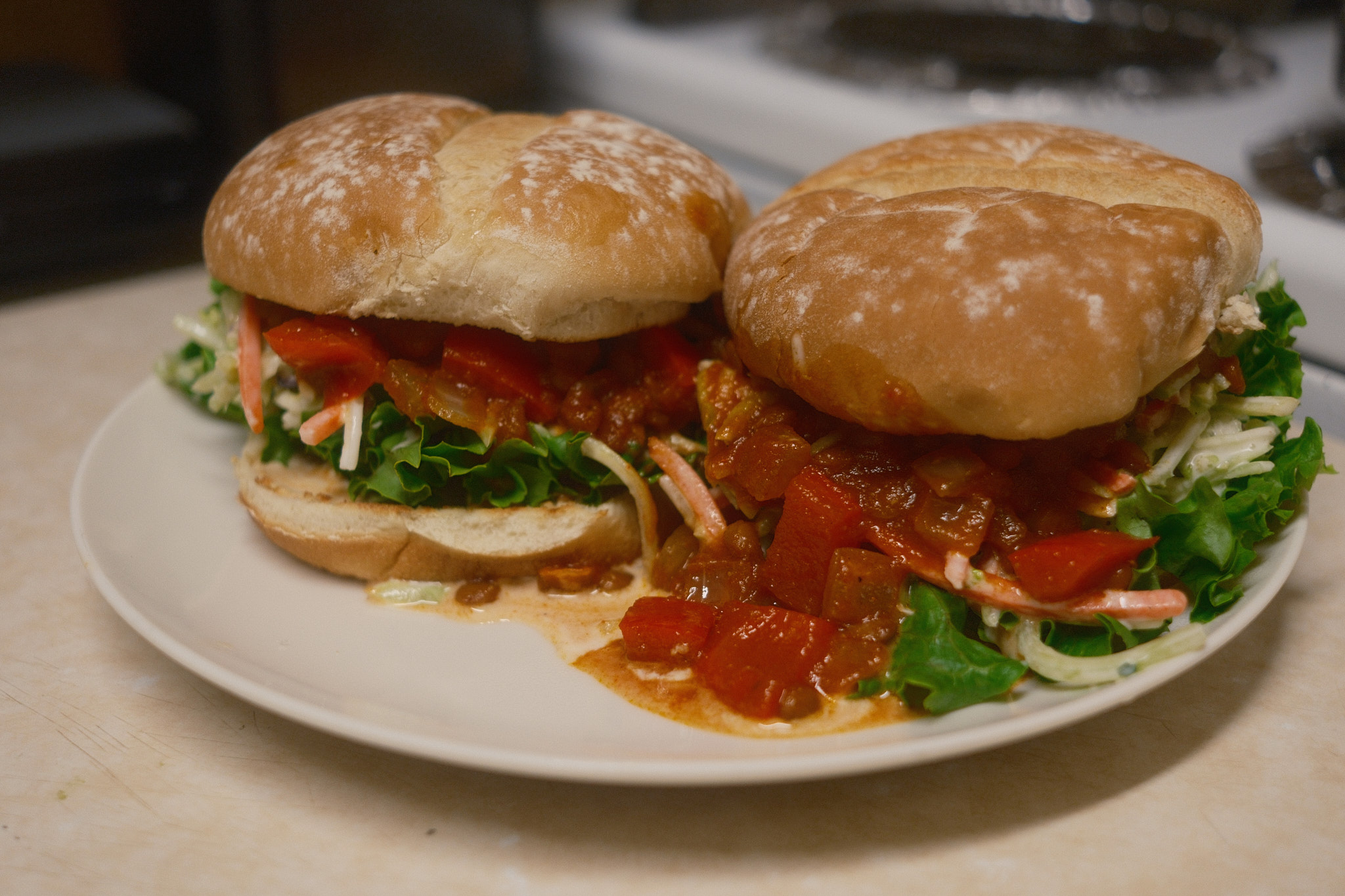 Two vegan sloppy joe burgers on a plate, the lentil tomato mixture oozing onto the plate