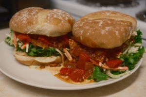 Two vegan sloppy joe burgers on a plate, the lentil tomato mixture oozing onto the plate