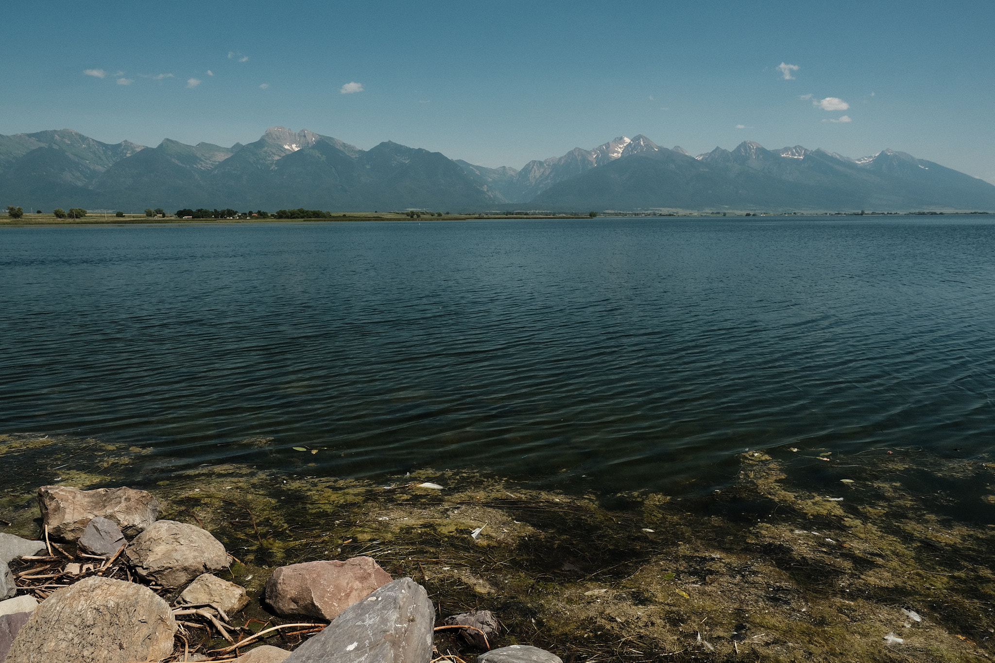 a sunny day at the Ninepipes Reservoir, the mountains off in the distance, the water gently waving onto some rocks