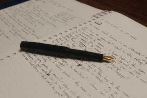 a couple of notebook pages with Italian language study notes written in black ink with a fountain pen, the pen lying flat and uncapped over the pages, the golden nib facing the camera