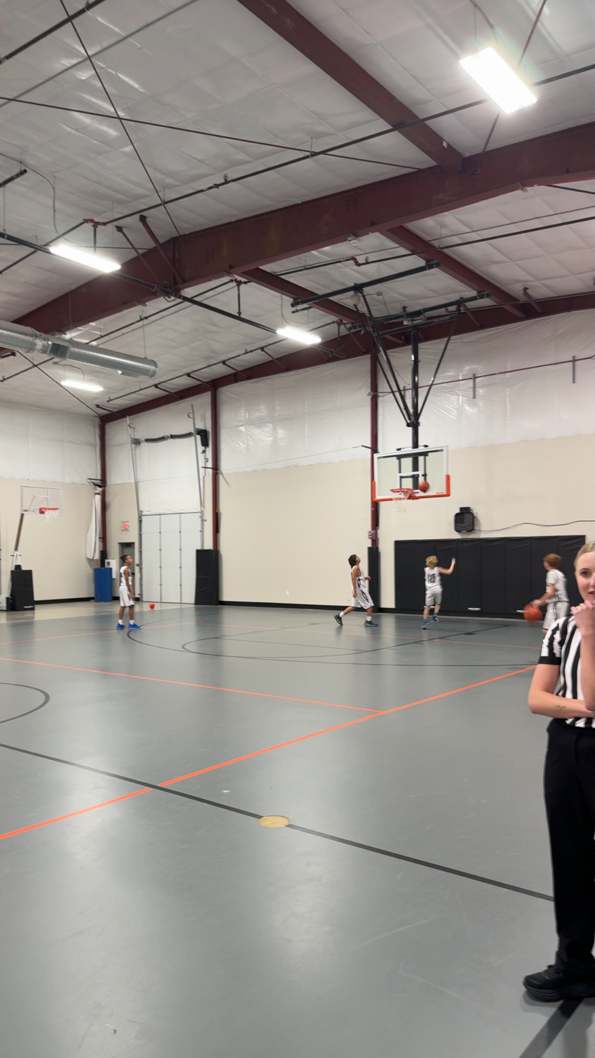 A group of middle school aged boys shooting hoops in an indoors basketball court