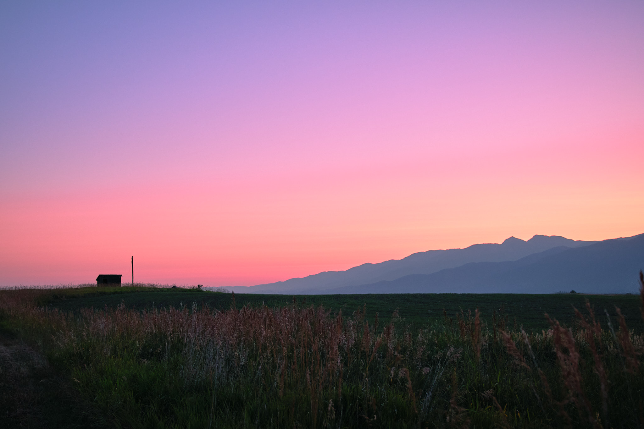 An early morning sunrise, a small structure on a green hill, the purple mountains off to the right, the sky a spectrum of pinks, reds, yellows, and purples